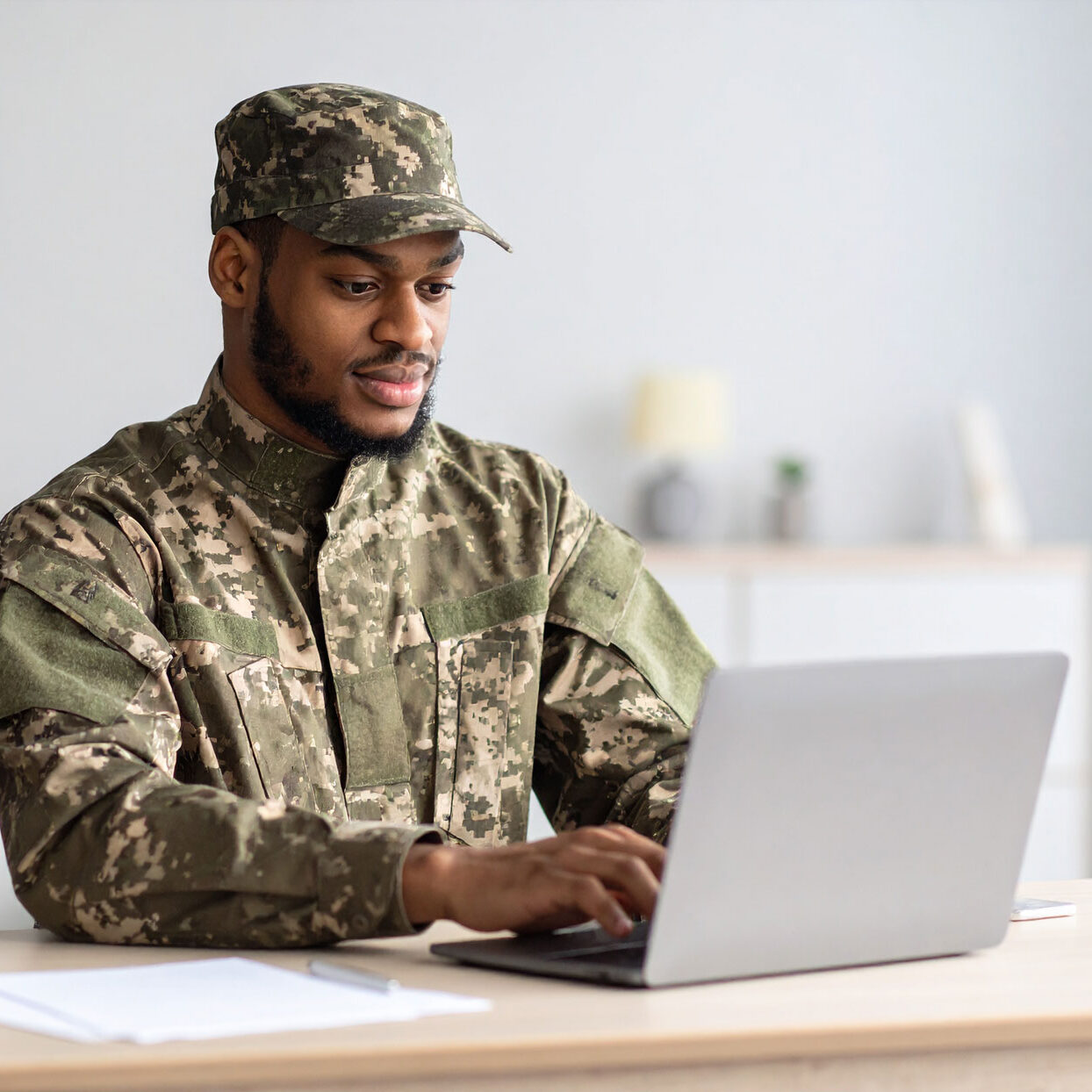 man-on-military-uniform-searching-the-web-on-a-laptop,-seating-on-a-table-at-home man-on-military-uniform-searching-the-web-on-a-laptop,-seating-on-a-table-at-home